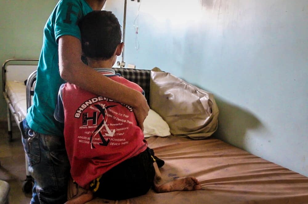 Nine-year-old Abdul Hadi is hugged by his older brother in a hospital ward in besieged east Aleppo. He needs a CT scan, but the equipment is not available, and he cannot be referred elsewhere for specialised care because all roads leading out of the city are blocked. Photo credit: Thaer Mohammad/MSF