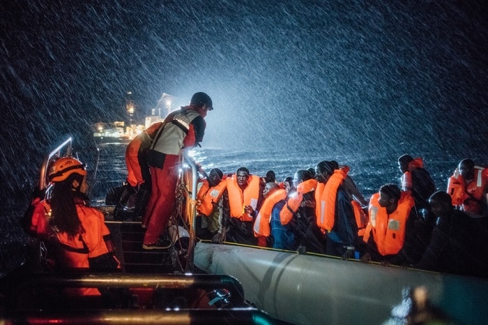 Rescuers from SOS Mediterranee, with whom MSF partners on board the search and rescue ship&nbsp;Aquarius, distribute lifejackets in heavy seas and pouring rain to refugees adrift on a small inflatable boat in the Mediterranean Sea.