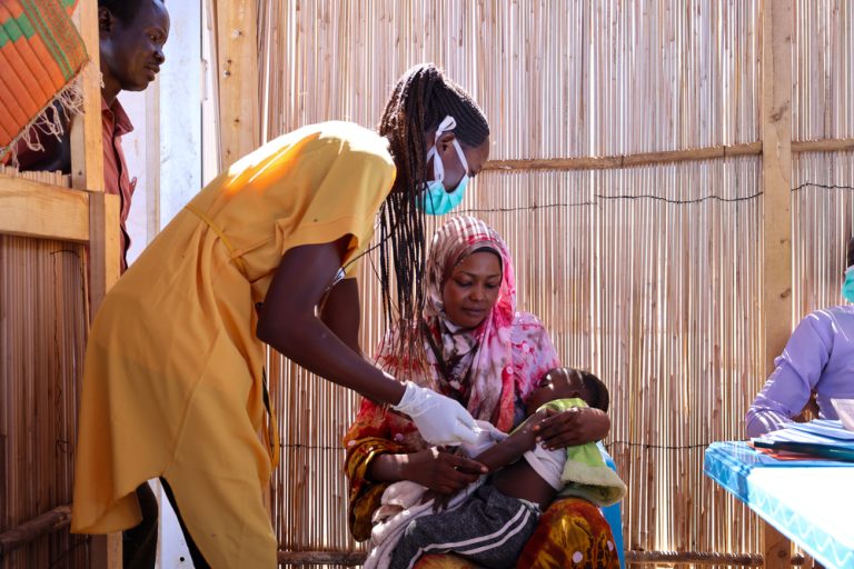 Halima Abdurahman Dawud is holding her daughter Aszed Mohammed, who is receiving a vaccine at the distribution site in Renk, Upper Nile. Halima is a refugee from Sudan who came looking for safety in Renk; she bought her daughter for vacation at the MSF vacation site at the transit centre. MSF provide vaccines to children who left Sudan without vaccination or incomplete vaccines.