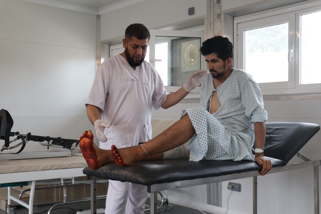An MSF physiotherapist helps a patient with leg exercises in the physiotherapy department of the MSF Trauma Centre in Kunduz Province. Baryali, 23, sustained a gunshot wound to his left leg, resulting in a fractured femur that was treated with external fixation. ©️ Tasal Khogyani/MSF