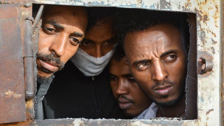 Refugees in Zintan DC at the gate of the main warehouse where 700 of them were detained. 
A tuberculosis outbreak has likely been raging for several months in the detention centre and some wear masks for fear of contamination. 
The main warehouse was emptied in June 2019, and the remaining people distributed among the other buildings within the detention centre compound.